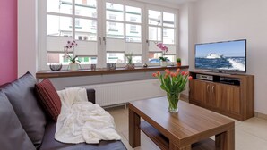 Una sala de estar con un sofá, una mesa de centro, un televisor sobre un mueble de madera y una ventana con persianas.