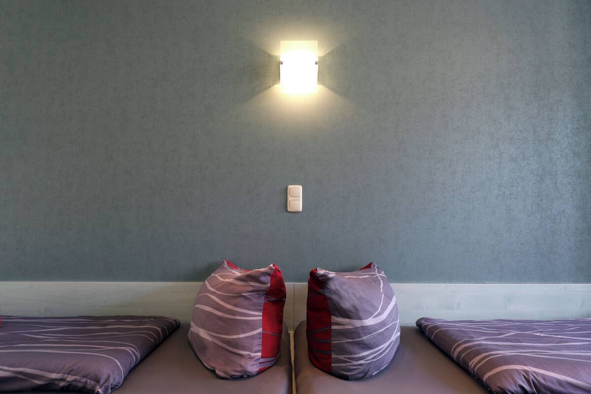 Une chambre avec deux lits, chacun agrémenté de draps à rayures et de touches de couleur rouge. On peut voir un luminaire fixé au mur au-dessus des lits.