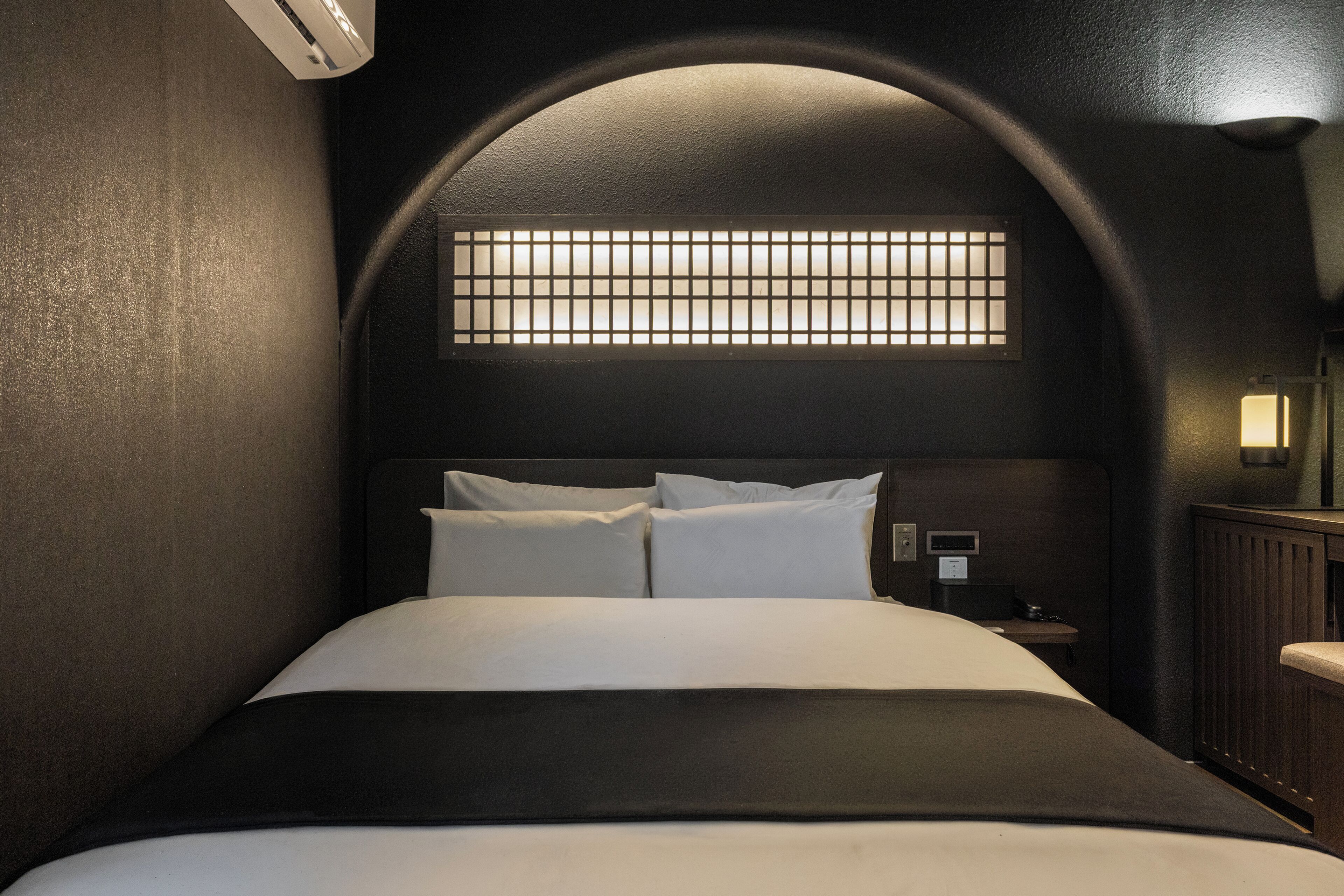 A bed with a headboard, a bedside table, and a wall-mounted light fixture.