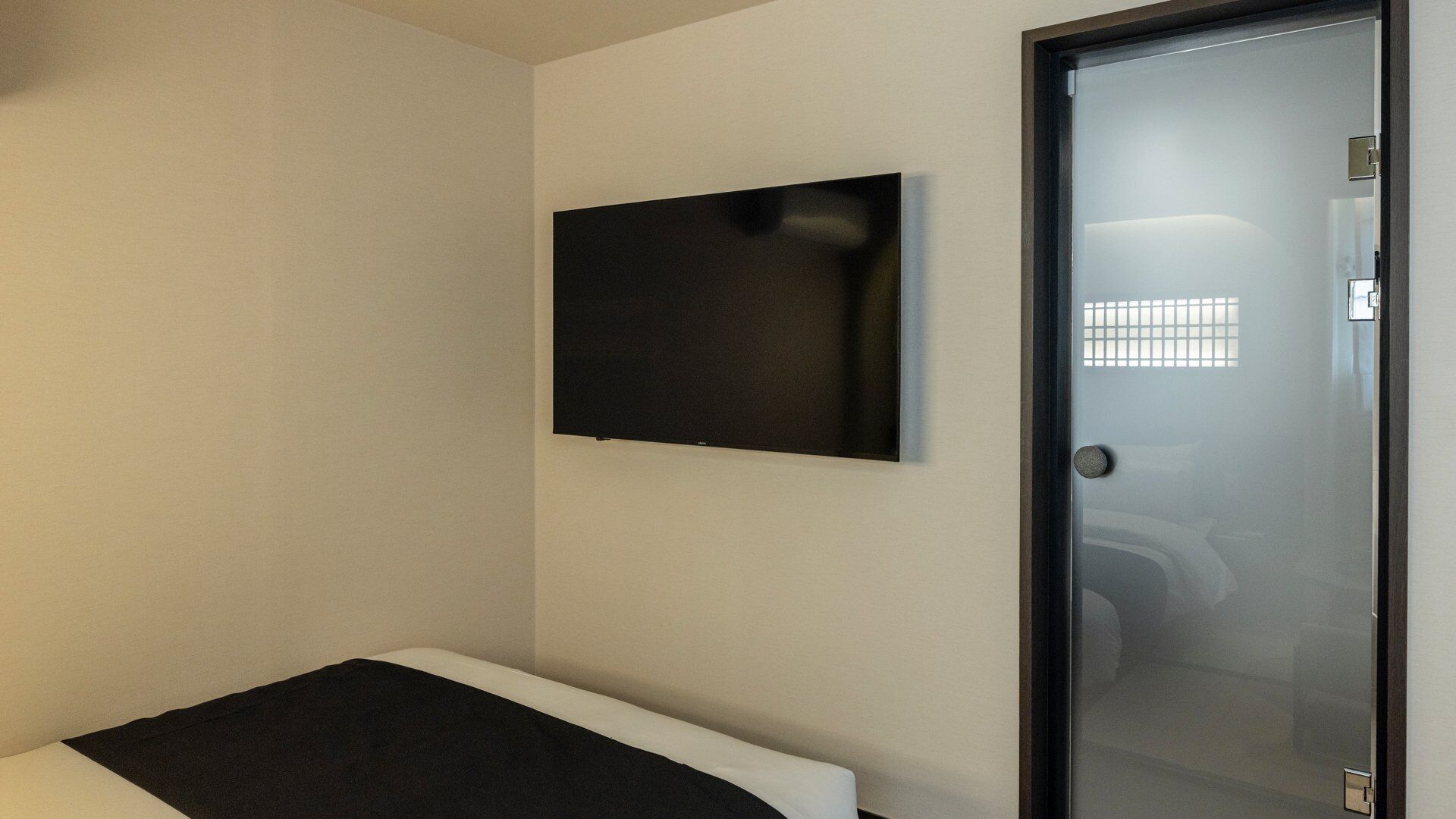 Una habitación con una cama, un televisor de pantalla plana montado en la pared y una puerta con un panel de vidrio satinado.