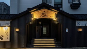 L'ingresso di un hotel con una facciata scura, un cartello con la scritta 'Ryokan Hotel Cave by Aonok' e dei gradini che conducono all'ingresso.