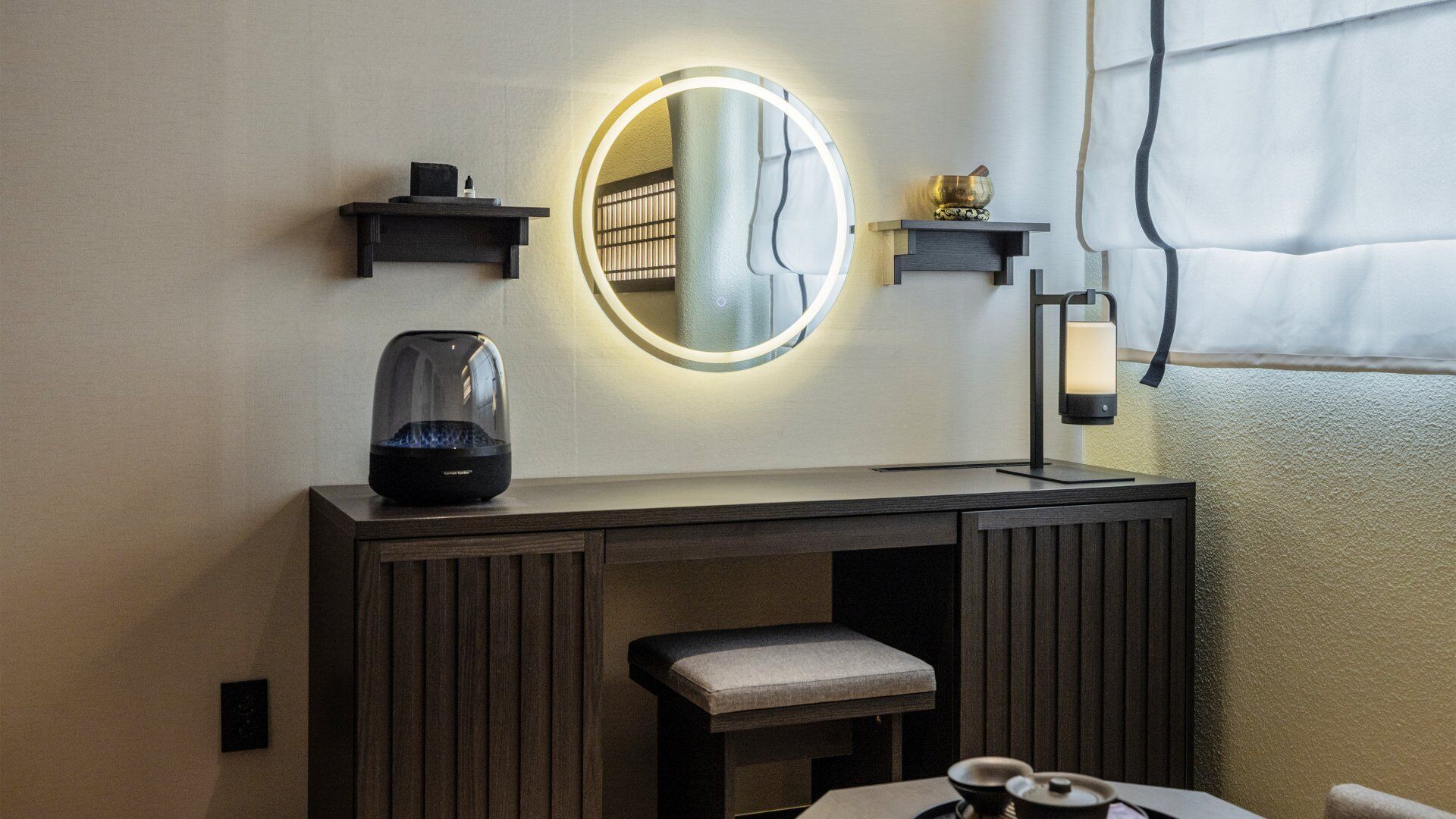 Un baño moderno con tocador, un espejo redondo con luces, hervidor de agua y un pequeño banco.