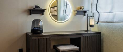 Un baño moderno con tocador, un espejo redondo con luces, hervidor de agua y un pequeño banco.