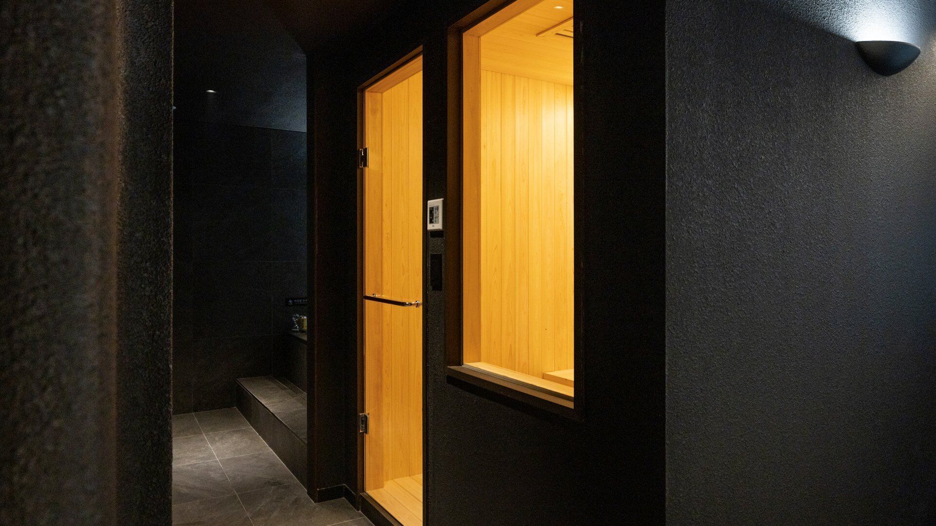 Un corridoio con una porta in legno e un punto luce a parete.