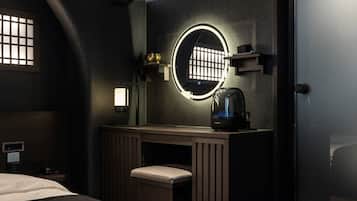 A hotel room with a wooden vanity, a round mirror, a kettle, and a bed.