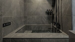 Un bagno moderno con doccia vetrata, piastrelle scure e un cartello di avvertimento.