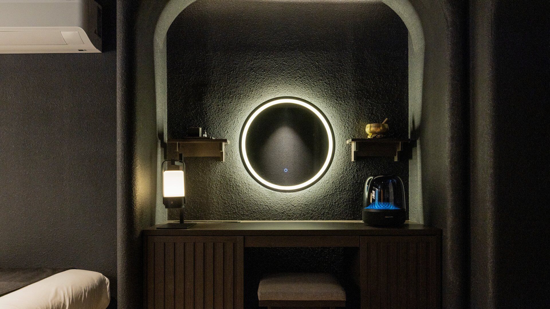 A bathroom with a round mirror, a light fixture, and a coffee maker.