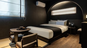 A modern hotel room with a bed, bedside table, chair, and a small table with a bowl.