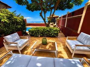 A poolside area with white outdoor furniture, a wooden table, and a view of the sea. - Villa Zen Adeje - Private Heated Pool (Adeje)
