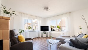 A modern living room with a fireplace, grey sofas, a flat-screen TV, and large windows with curtains. - Apartment 'Haus Am Idyllischen Bach' with Private Garden and Wi-Fi (Rheinau)