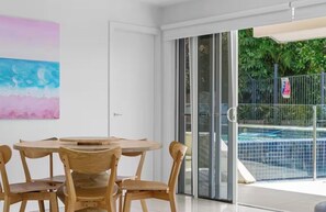 A dining area with a table and chairs, a glass door leading to a pool area, and a painting on the wall. - AcquaVista (Terrigal)