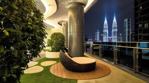 Een dakterras met uitzicht op de Petronas Towers, een bloempot en een rieten loungestoel.