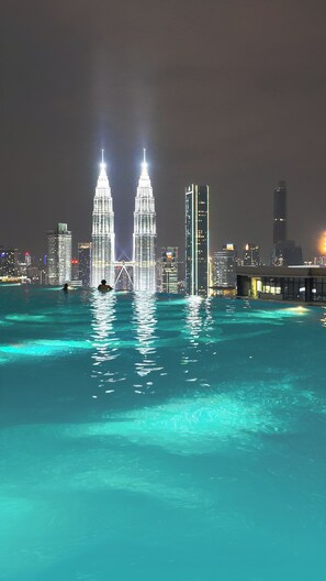Paesaggio urbano notturno con due torri illuminate, un ponte e uno specchio d'acqua che riflette le luci.