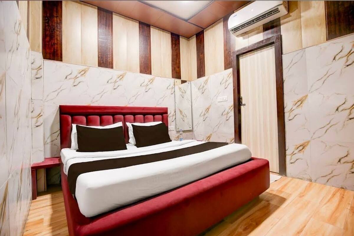 Un dormitorio con una cama tapizada en rojo, paredes con estampado de mármol y suelo de madera.