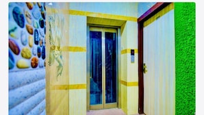 Un ascensor con puertas de vidrio, una pared con diseño decorativo y una pared de césped artificial verde.
