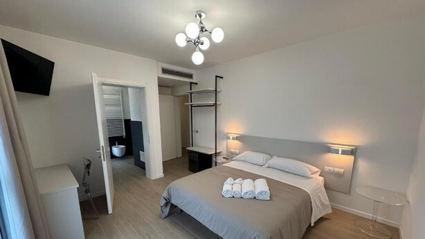 A bedroom with a bed, a bedside table, a wardrobe, a mirror, and a TV mounted on the wall. - HOTEL VILLA MARY (Santa Maria di Sala)