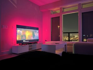 A modern living room with a flat-screen TV, a white sofa, and a large window overlooking a cityscape. - Cozy contemporary & chic Deep Ellum apartment in Dallas’s nightlife district (Dallas)