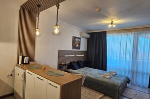 A hotel room with a bed, a desk with a kettle, a mirror, and a window with curtains. - Premium Studio • SPA & Pools • Fitness • Free Parking (Ravda)
