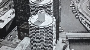 Un edificio de gran altura con un diseño circular distintivo, rodeado de otros rascacielos y un río.