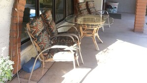 Un patio con una mesa de vidrio, sillas de mimbre, un arco de ladrillo y una planta en maceta.
