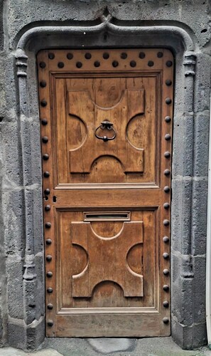 A wooden door with a metal handle and decorative elements, set in a stone wall.