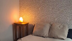 Een bed met een gebreide deken, een bedlampje en behang met een patroon.