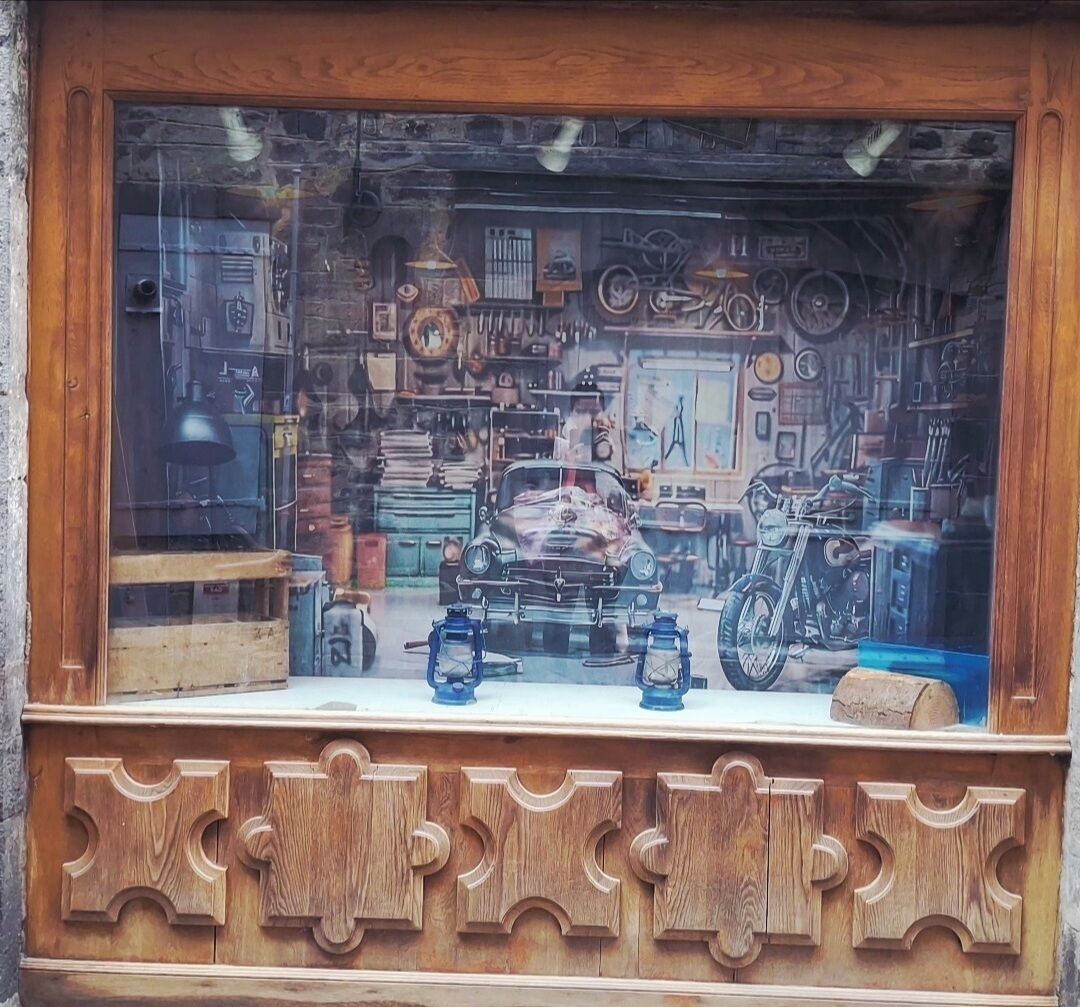 Un escaparate con un coche antiguo, faroles y varias piezas mecánicas.