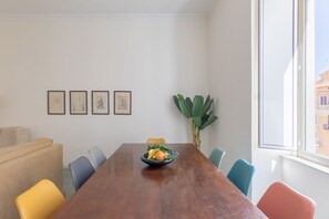 A dining area with a wooden table, colorful chairs, a bowl of fruit, framed pictures on the wall, and a large plant. - iFlat | Calm & Spacious Urban Oasis Fons Trevi B13 (Rome)