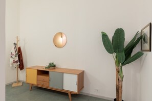 A minimalist room with a wooden cabinet, a round wall light, and a large plant. - iFlat | Calm & Spacious Urban Oasis Fons Trevi B13 (Rome)