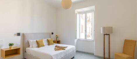 A bedroom with a bed, bedside table, lamp, chair, and a window.