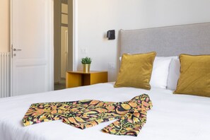 A hotel room with a bed, a bedside table with a plant, and a wall-mounted light. - iFlat | Calm & Spacious Urban Oasis Fons Trevi B13 (Rome)