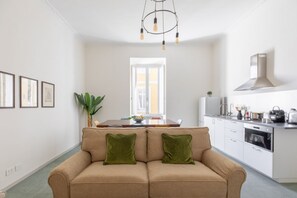 A modern kitchen with white cabinets, a stainless steel range hood, and a dining area with a table and chairs. - iFlat | Calm & Spacious Urban Oasis Fons Trevi B13 (Rome)
