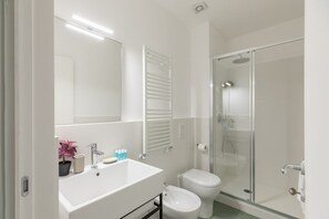 A bathroom with a white sink, mirror, toilet, and glass shower enclosure. - iFlat | Calm & Spacious Urban Oasis Fons Trevi B13 (Rome)