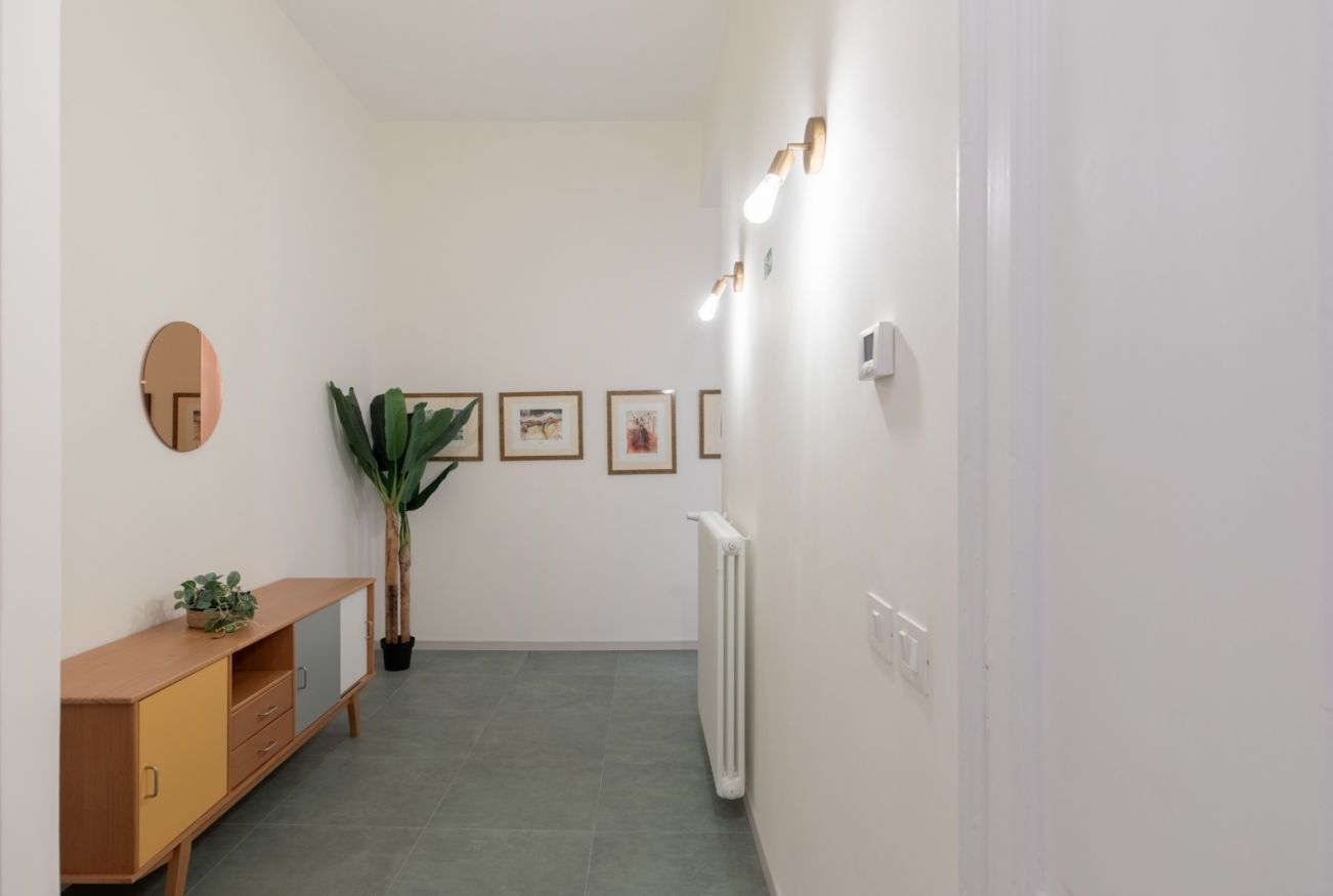 A hallway with a radiator, a potted plant, framed pictures on the wall, and a wooden cabinet.