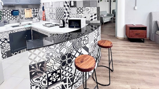 Een moderne keuken met een decoratieve spatwand, een centraal eiland met barkrukken en hanglampen.