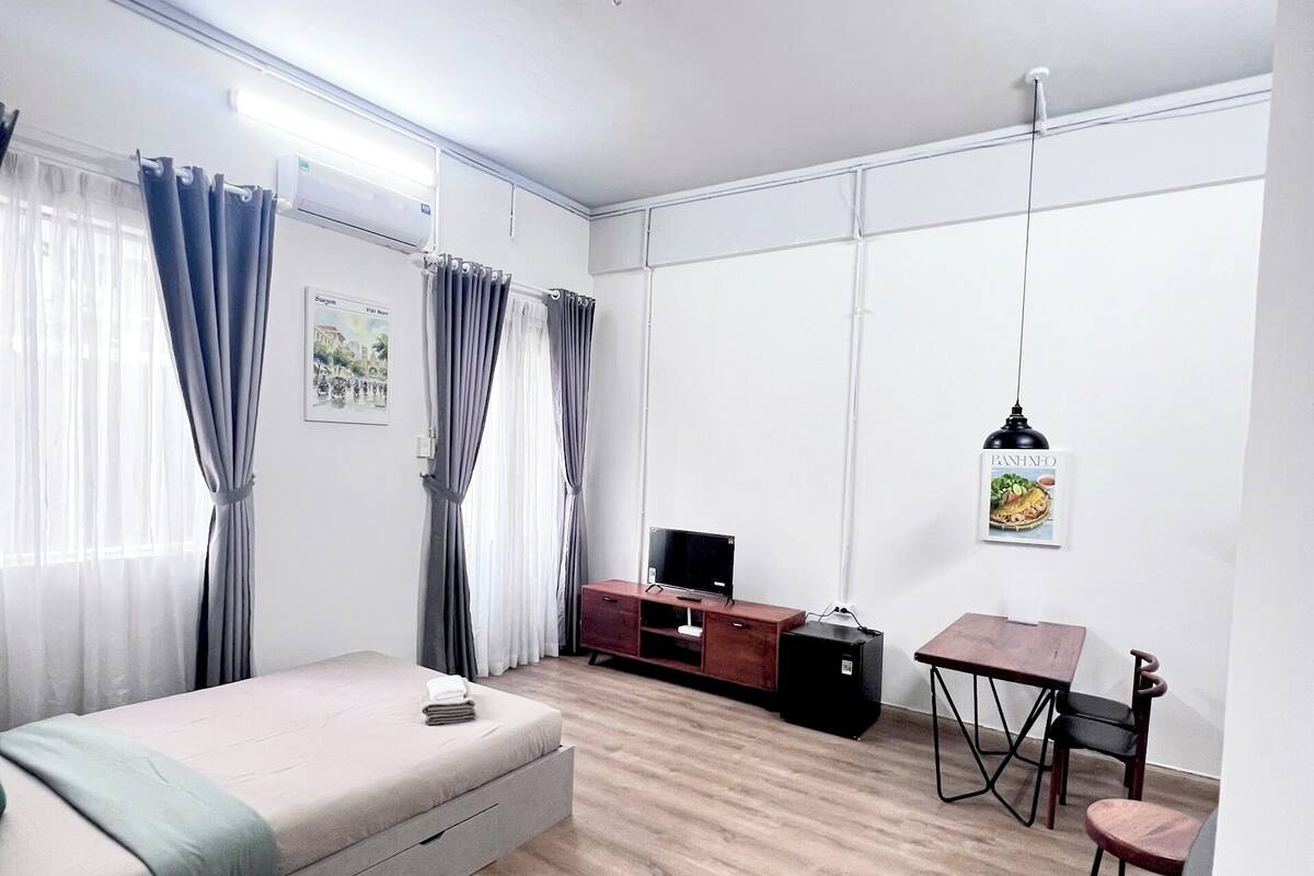 Ein modernes, gut beleuchtetes Zimmer mit einem Bett, einem Fernseher, einem kleinen Esstisch und einem Schreibtisch.