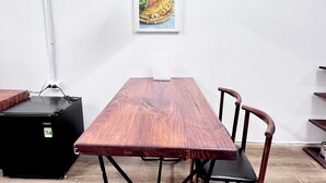 Een eetruimte met een houten tafel, zwarte metalen poten, een zwarte hanglamp en een lijst met het menu aan de muur.