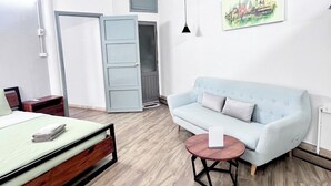 Een moderne slaapkamer met een bed, een lichtblauwe bank, een ronde houten salontafel en een stadsgezichtschilderij aan de muur.