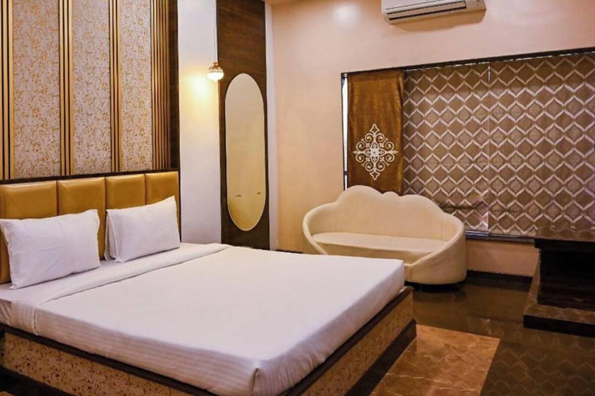 A hotel room with a large bed, a seating area, a wall-mounted air conditioner, and a patterned wall.