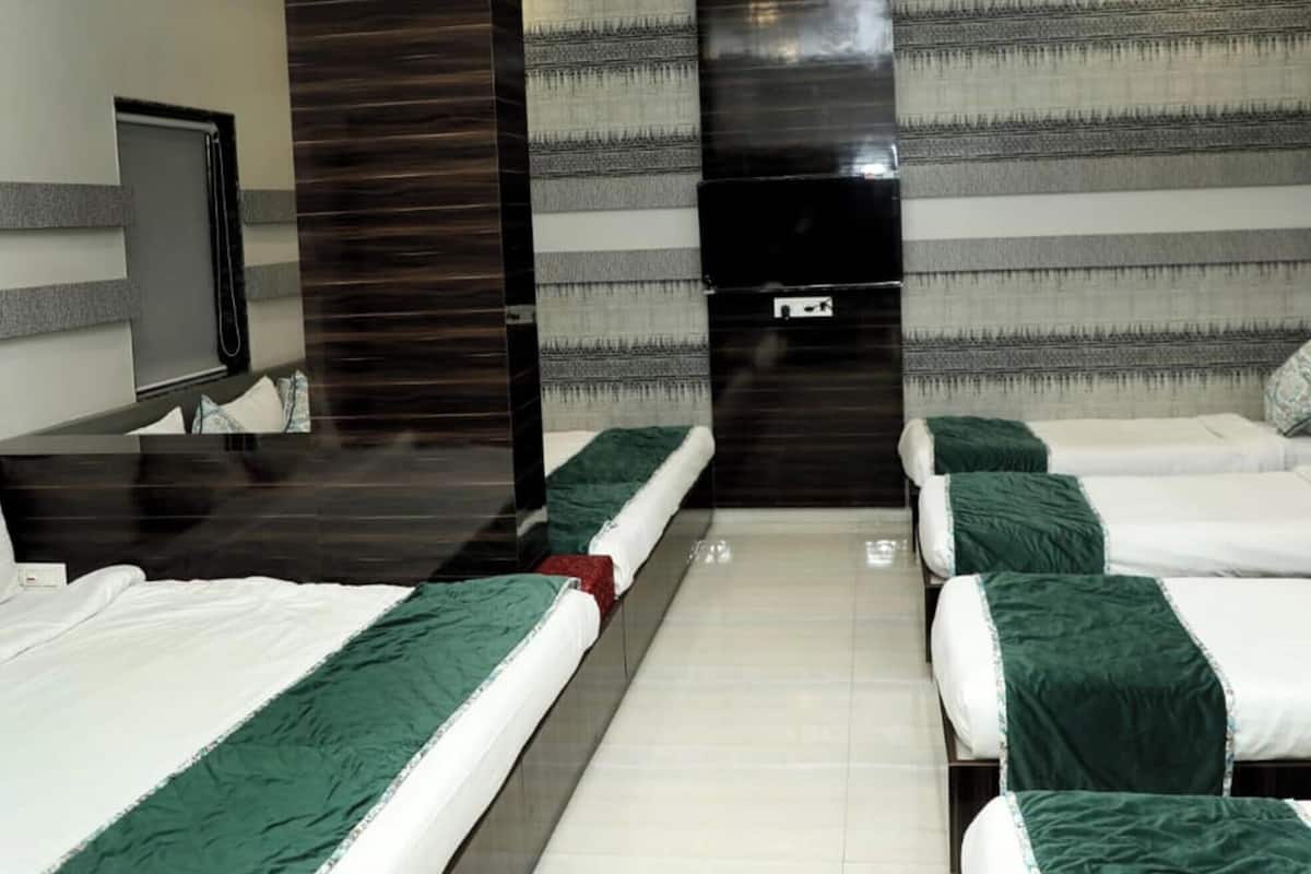A hotel room with three beds, a dark wooden headboard, a large mirror, and a striped wall.