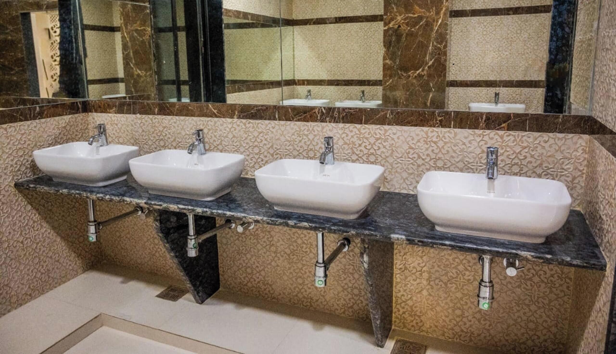Une salle de bain avec trois lavabos, un mur en marbre et un miroir.