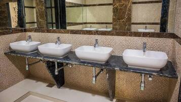 Une salle de bain avec trois lavabos, un mur en marbre et un miroir.
