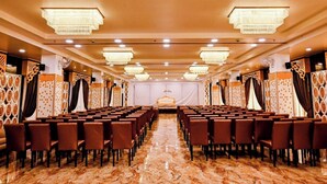 Una sala conferenze con file di sedie, lampadari e tende a motivi decorativi.
