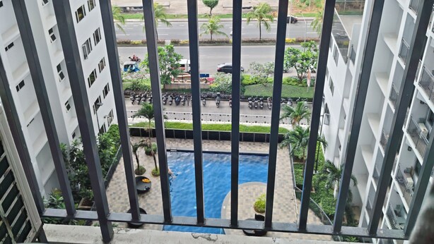 Un balcón con vistas a una piscina, edificios cercanos y una calle concurrida.