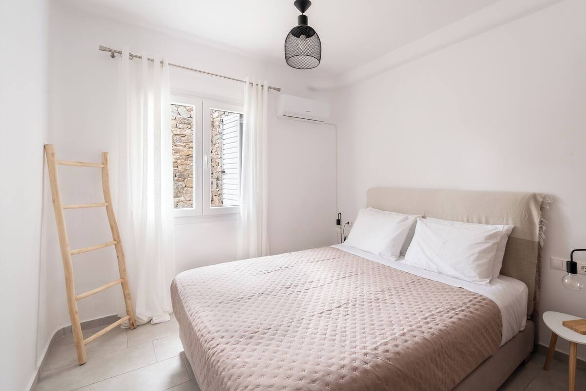 Quarto com cama, escada, janela com persianas, ar condicionado e mesa de cabeceira com abajur.