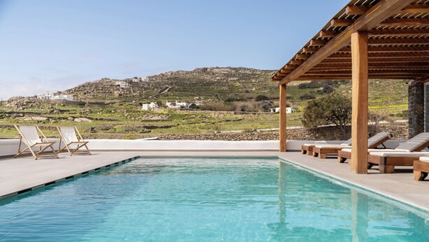 Una piscina con sillas de descanso, una pérgola y vistas a una colina con edificios.