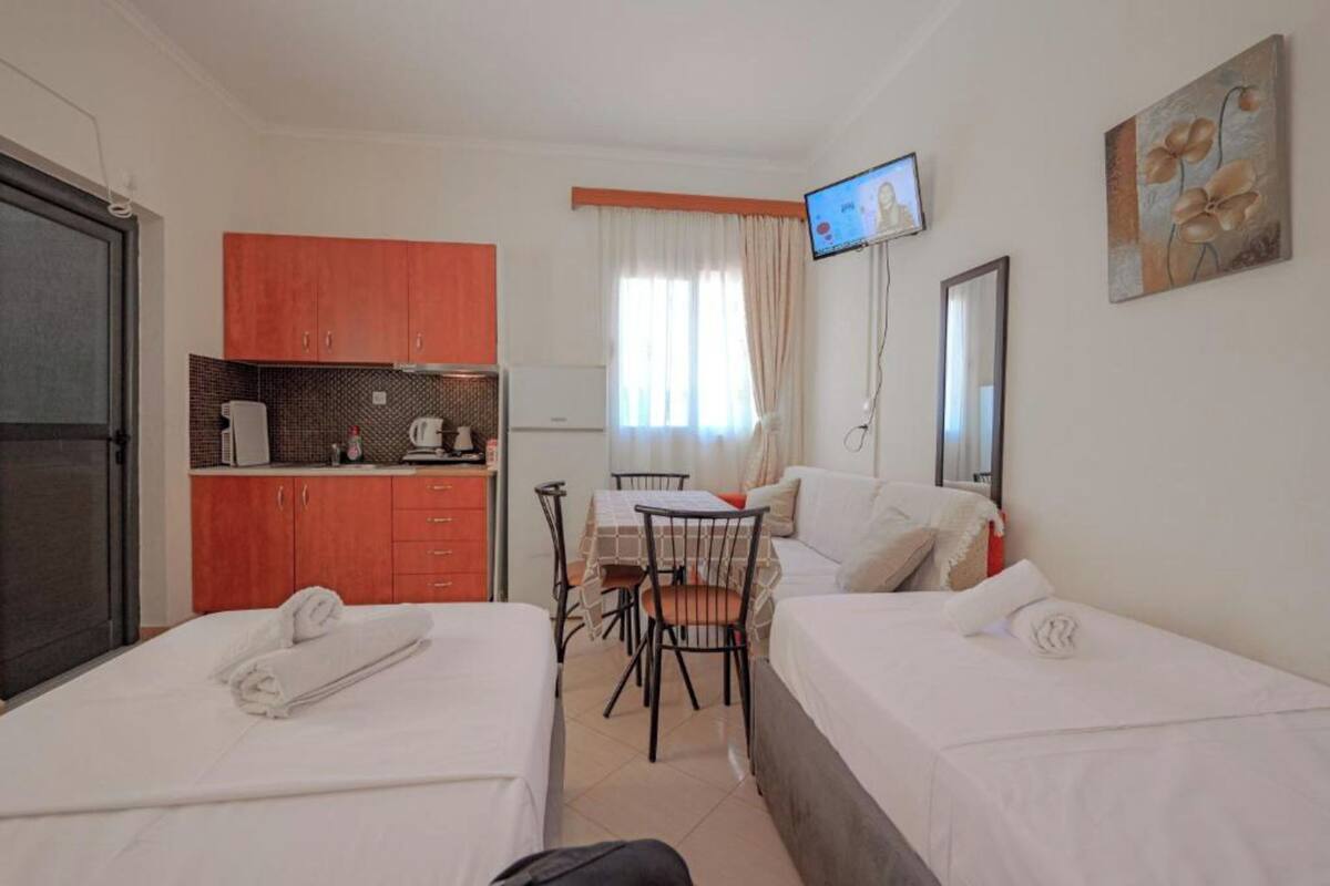 A hotel room with two beds, a kitchenette, a dining table with chairs, a TV, and a painting on the wall.