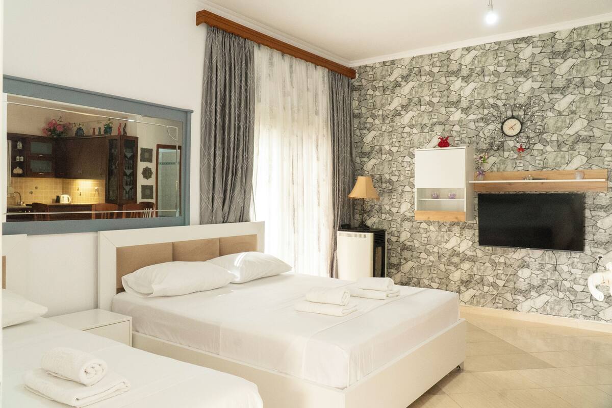 A hotel room with a bed, a TV, a stone wall, a mirror, and a small shelf.