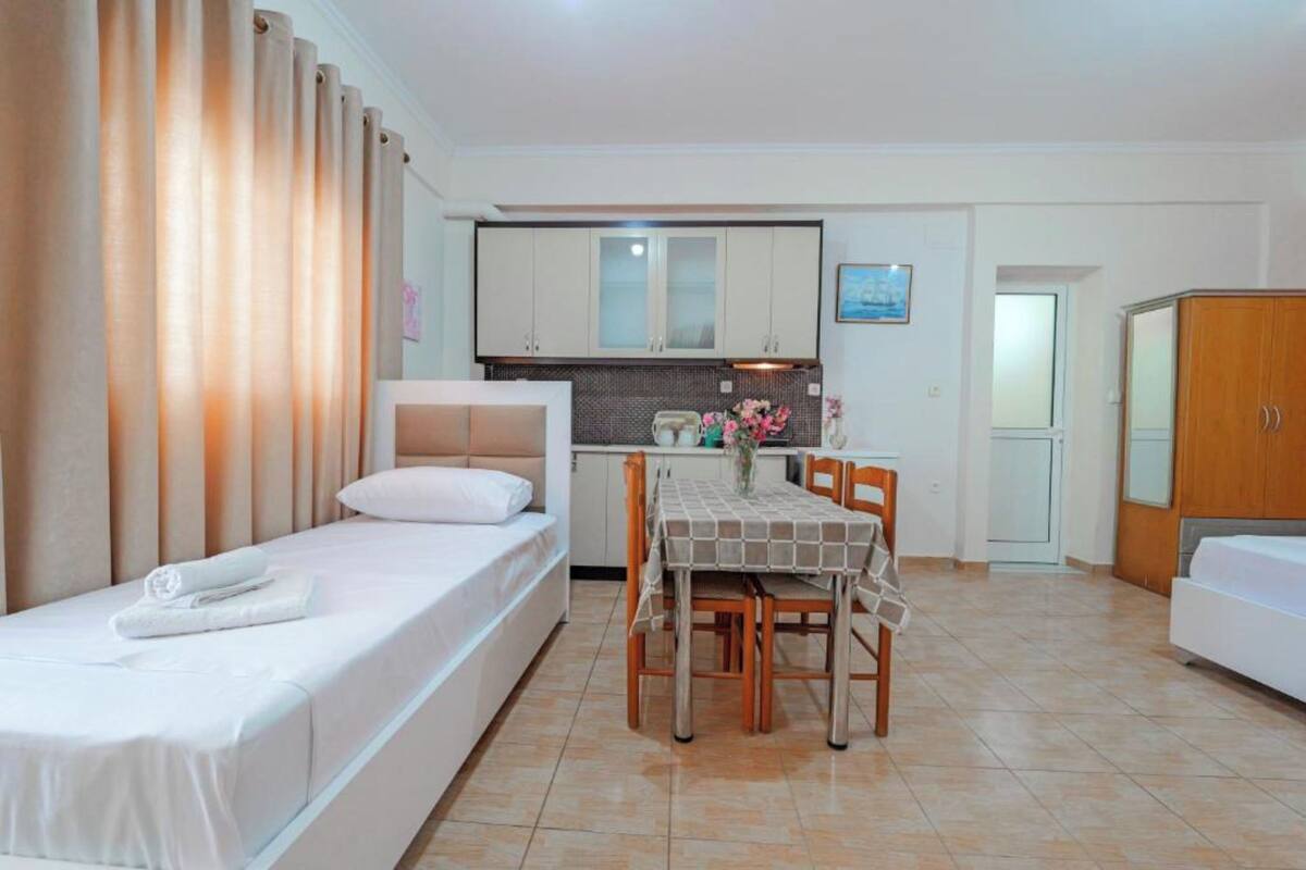 A bedroom with a bed, a small table with chairs, a kitchenette, and a bathroom.
