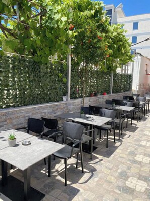 An outdoor patio with tables and chairs, a stone wall, and a climbing plant with red berries. - Villa Rafail (Ksamil)
